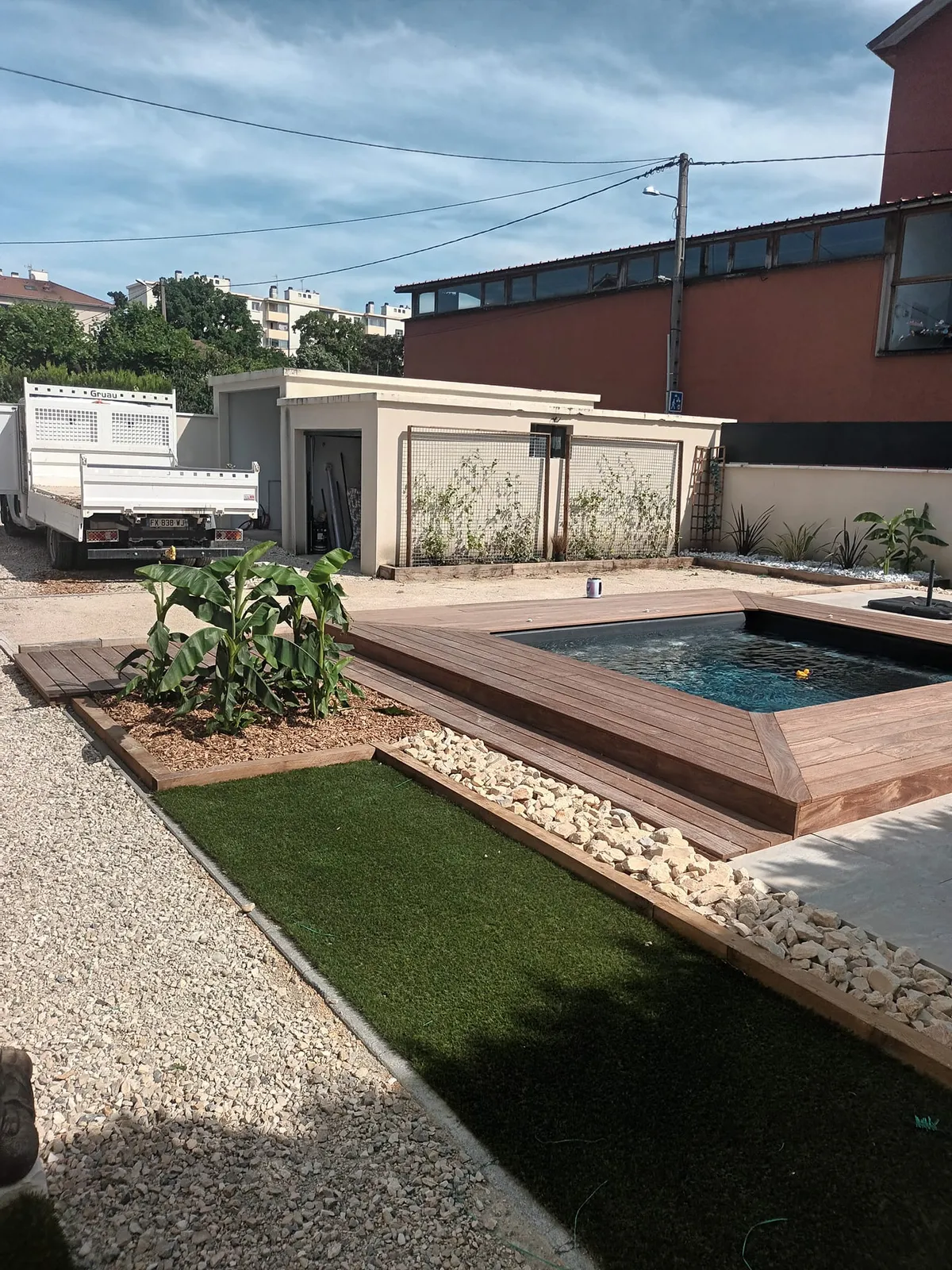 Piscine avec plage en bois, gravier blanc et bandes de gazon