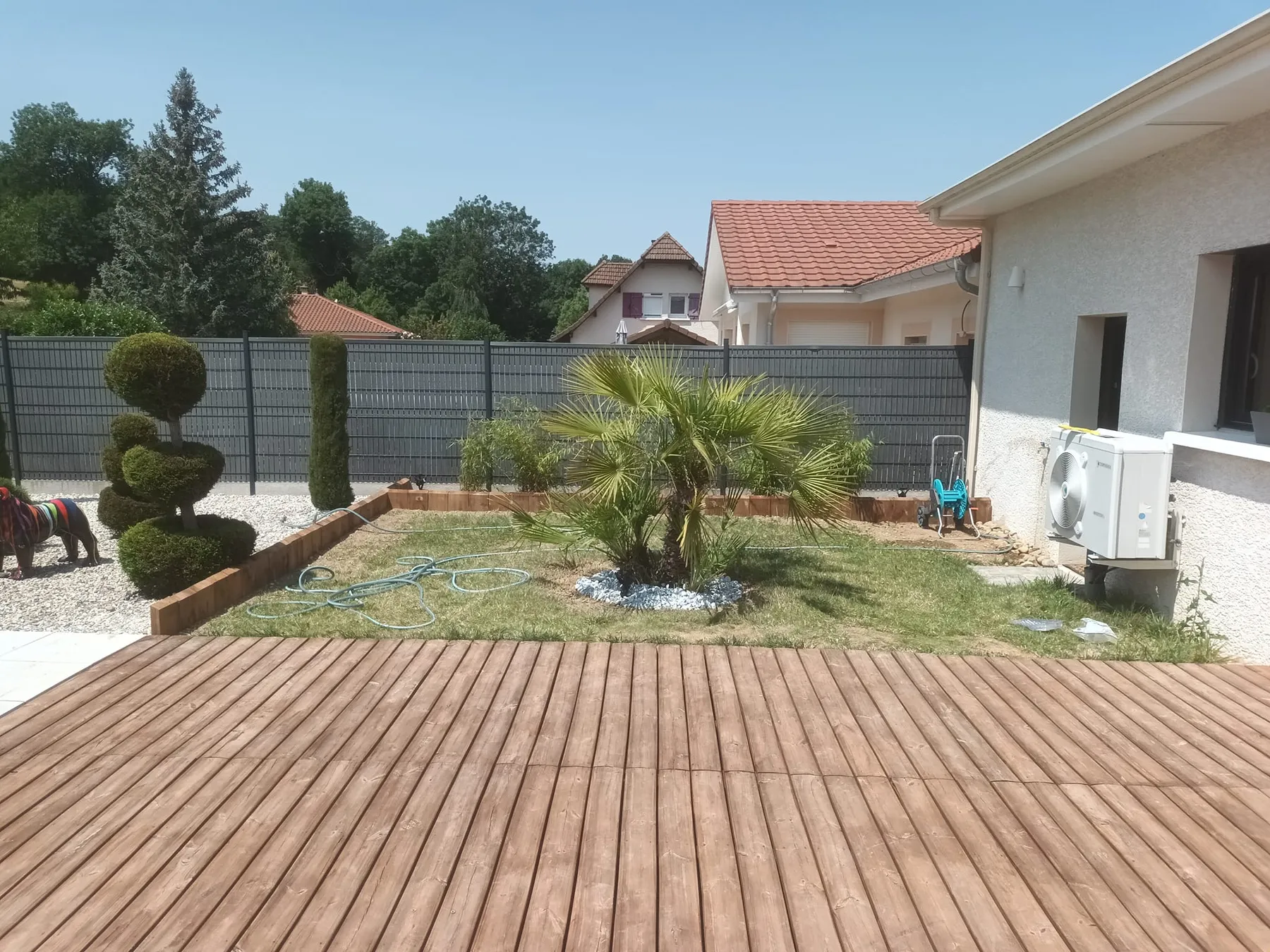 Terrasse en bois, topiaires taillés et palmier dans un jardin clos