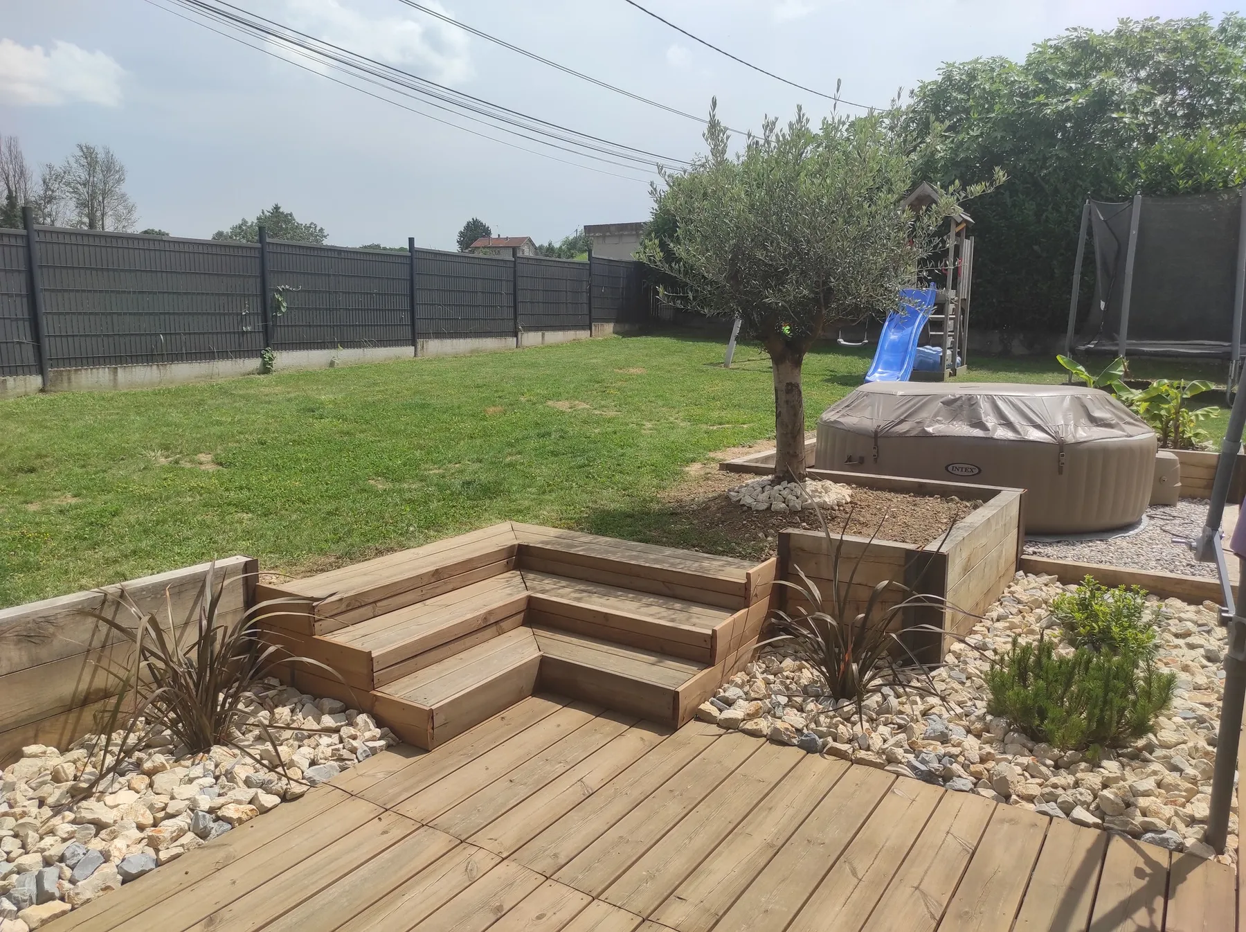 Terrasse en bois avec emmarchement, spa, massif de galets et olivier