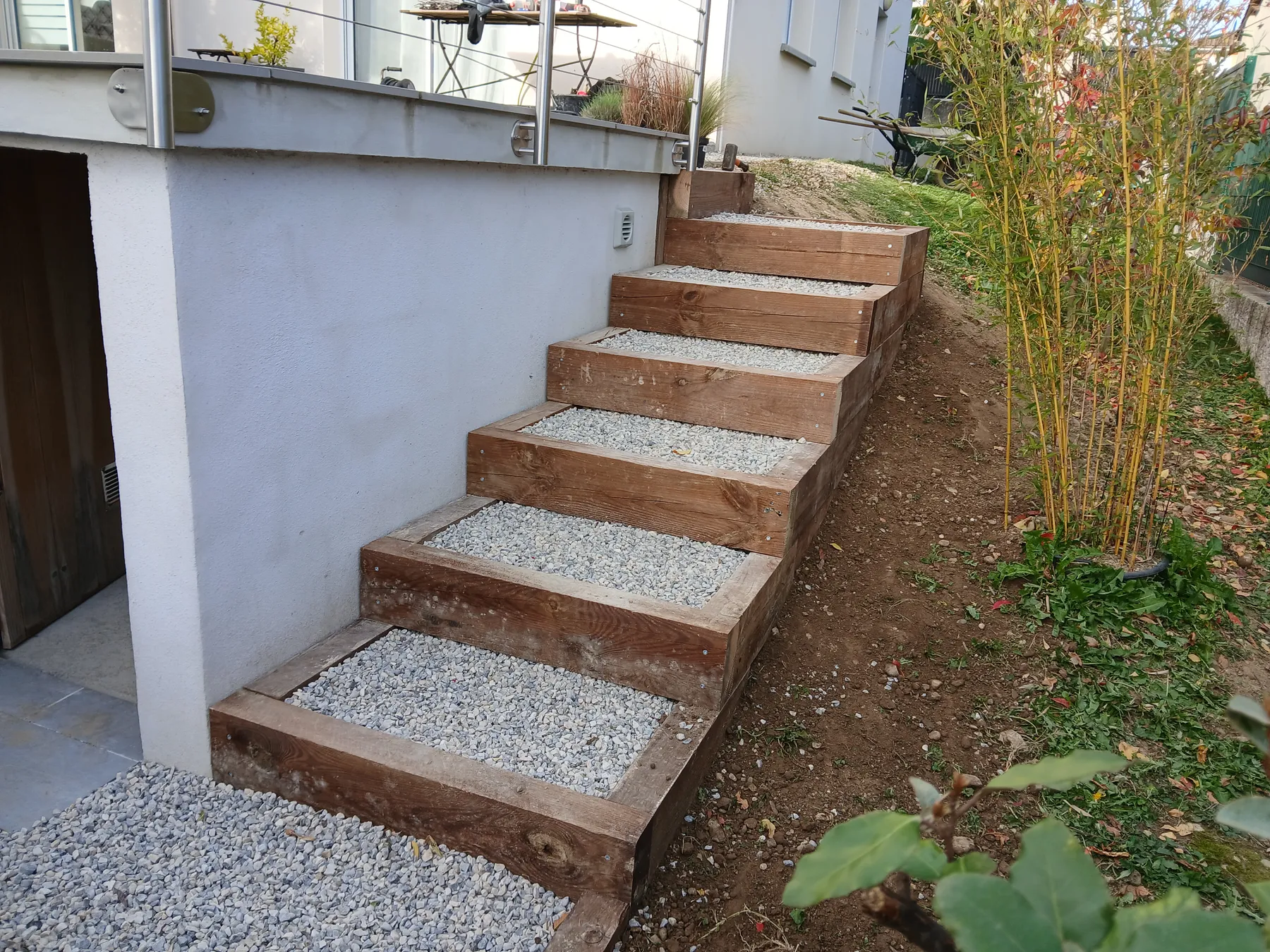 Escalier extérieur en traverses de bois à marches garnies de gravier, le long d’un mur enduit